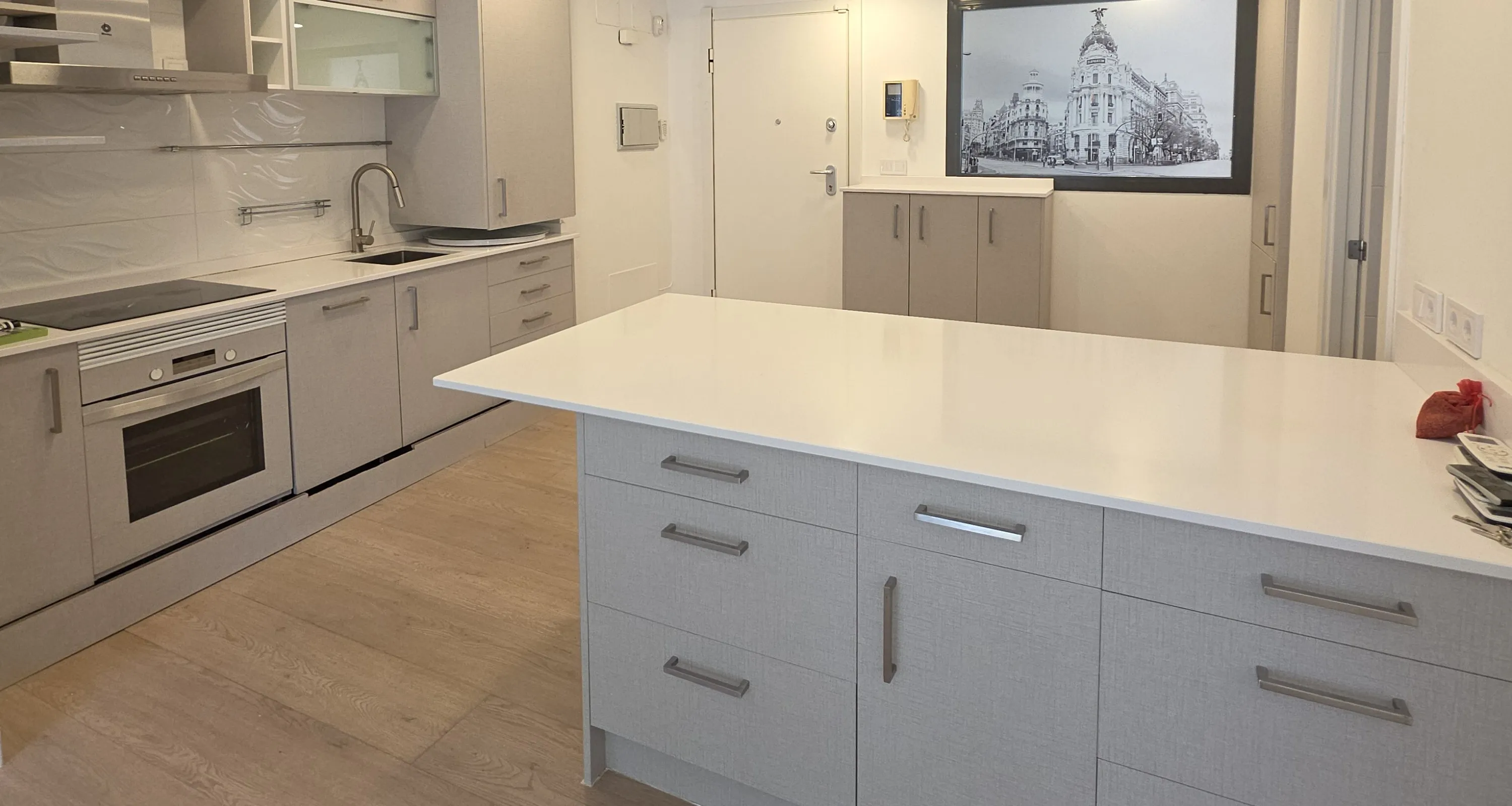 Cocina abierta con isla y muebles revestidos con vinilo gris de textura textil en una vivienda de Madrid